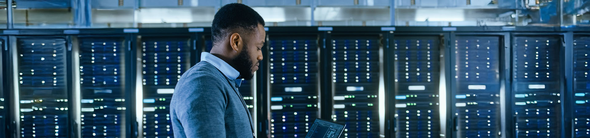 Man standing in a server room looking at a laptop